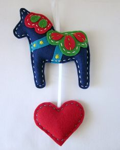 a felt horse ornament hanging on a white wall next to a red heart