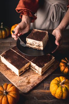 a person holding a knife and fork over some desserts on a wooden cutting board