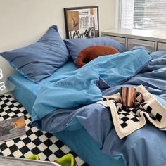 an unmade bed with blue sheets and checkered rugs on the floor next to a window