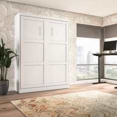 a room with a desk, chair and large white cupboards in front of a window