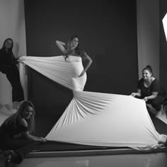 a group of women posing in front of a white backdrop with the woman's dress draped over her shoulders