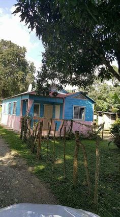 a small blue and pink house sitting in the middle of a yard next to trees