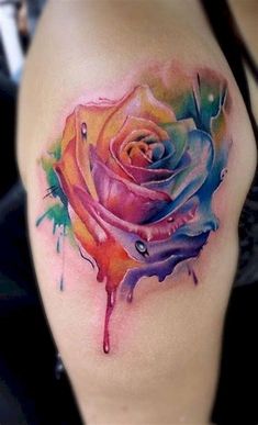 a colorful rose tattoo on the side of a woman's thigh, with watercolor splashes