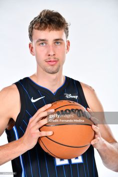 a young man holding a basketball in his right hand and looking at the camera with a serious look on his face