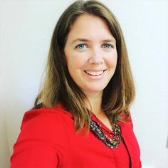 a woman in a red jacket is smiling at the camera while standing next to a white wall