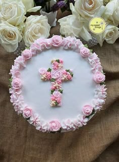 a cake decorated with pink flowers and a cross on it, surrounded by white roses