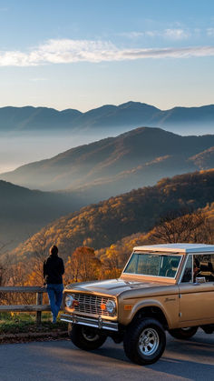 a person standing on the side of a road next to a car with mountains in the background