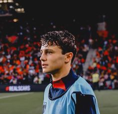 a young man standing on top of a soccer field in front of an orange and black crowd