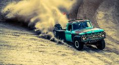 an old pickup truck driving down a dirt road with dust coming out of the bed