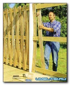 a man standing next to a wooden fence with his hands on the board and hammer