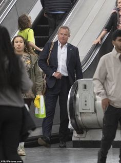 people are walking down an escalator with their luggage on the ground and one man is wearing a suit