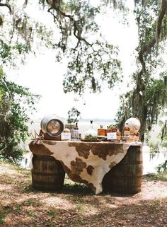 a cow skin covered table in the middle of a forest with lots of food on it