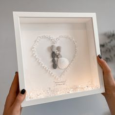 a woman holding up a white heart shaped shadow box with seashells in it