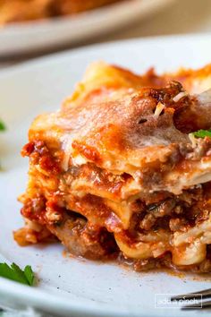 a white plate topped with lasagna covered in sauce and meaty toppings