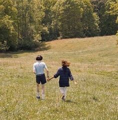 two children are holding hands while walking through a field with trees in the back ground