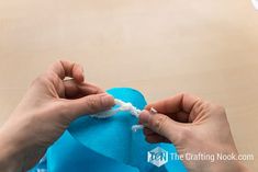 two hands are removing the fabric off of a blue stuffed animal that is sitting on a table