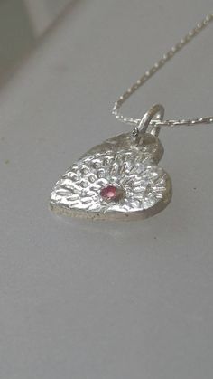 Made to Order: Handmade by Alison and finished by yours truly. Natural ruby (heat treated but not glass filled). Round cut with carat weight of 0.08ct that is bezel set. Lines lead out from ruby like a starburst. Pendant measures approximately 0.57 inches from top to bottom and 0.47 inches wide. Birthstone for July. Made of solid fine silver and comes with 18 inch sterling silver Cardano style chain with lobster clasp. Ruby Heart Pendant Jewelry For Anniversary, Heart-shaped Jewelry With Bezel Setting For Valentine's Day, Heart-shaped Bezel Set Jewelry For Valentine's Day, Anniversary Ruby Jewelry With Heart Charm, Heart-shaped Ruby Birthstone Jewelry, White Gold Heart-shaped Jewelry With Bezel Setting, Silver Heart-shaped Jewelry With Bezel Setting, Silver Sterling Silver Heart Cut Birthstone Necklace, Silver Sterling Birthstone Necklace With Heart Cut