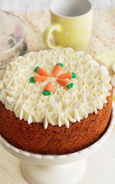 a cake with frosting and carrots sitting on a plate next to a cup