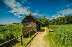 an old wooden shack sitting on top of a lush green field next to a dirt road