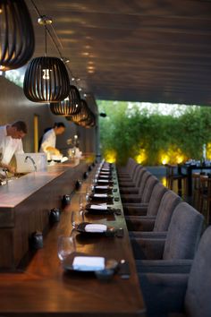 two chefs are preparing food at the counter in front of an open dining area with long wooden tables and gray chairs