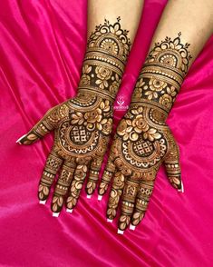 two hands with henna tattoos on them sitting on a pink cloth covered in satin