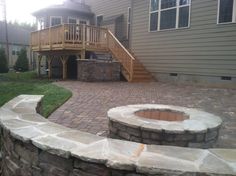 a brick patio and fire pit in front of a house with stairs leading up to the deck