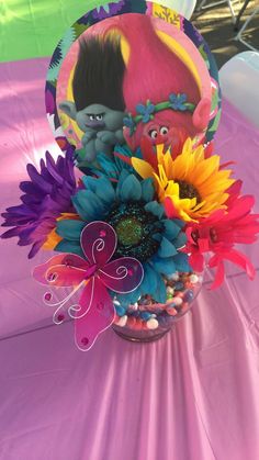 a vase filled with colorful flowers on top of a purple table cloth covered tablecloth