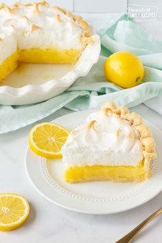 a slice of lemon meringue pie on a white plate next to a bowl of lemons