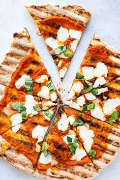 a pizza cut into four slices with cheese and basil on top, sitting on a white surface