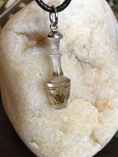 a small glass bottle sitting on top of a white rock next to a black cord necklace