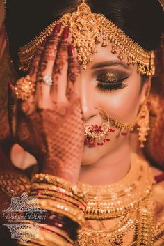 a woman with her hands on her face wearing gold jewelry and holding her hand up to her face