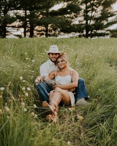 a man and woman are sitting in the tall grass with their arms around each other