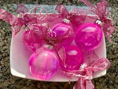 pink ornaments are on a white plate with ribbons and bows around them, sitting on a granite countertop