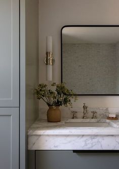 a bathroom sink sitting under a mirror next to a white cabinet and counter with flowers in it