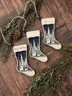 three christmas stockings hanging from a tree on top of a wooden floor with pine cones