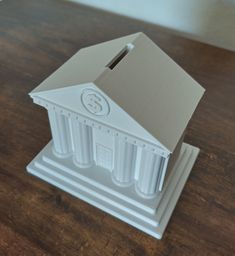 a small white building with columns and a clock on the top is sitting on a wooden table