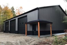 a large black building sitting on top of a dirt field next to trees and grass