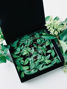 a black box with some green leaves and flowers in it on top of a table