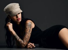 a woman with tattoos laying on the floor wearing a hat and black dress is posing for a photo