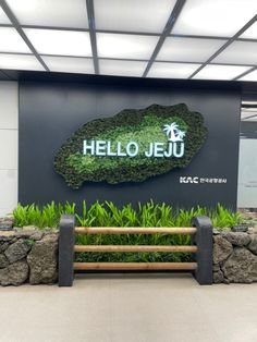 the entrance to hello jeju is decorated with green plants and rocks, along with a bench