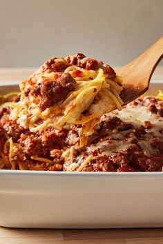 a wooden spoon full of spaghetti and meat casserole in a white dish on a table