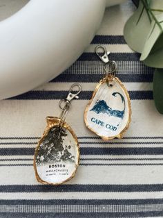 two key chains with the words cape cou printed on them sitting next to a potted plant