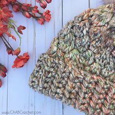 a crocheted blanket next to flowers on a white wooden surface