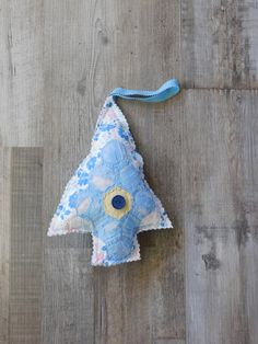 an ornament shaped like a christmas tree hanging on a wooden floor with a blue ribbon