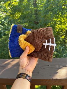 a hand holding a knitted football hat on top of a wooden bench in front of trees