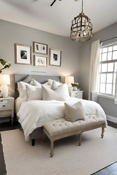 a white bed sitting under a chandelier in a bedroom next to a window