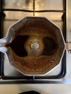 a coffee pot sitting on top of a stove next to a frying pan filled with liquid