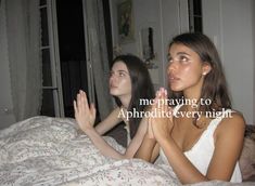 two young women sitting on a bed with their hands in the air and one is praying