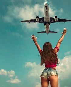 a woman standing in front of an airplane with her hands up to the sky above her head