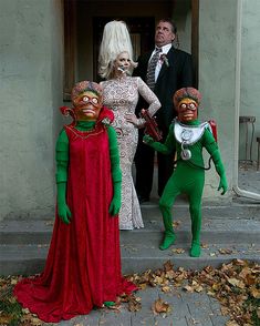 three people dressed up in costumes standing on the front steps of a house with two men and one woman